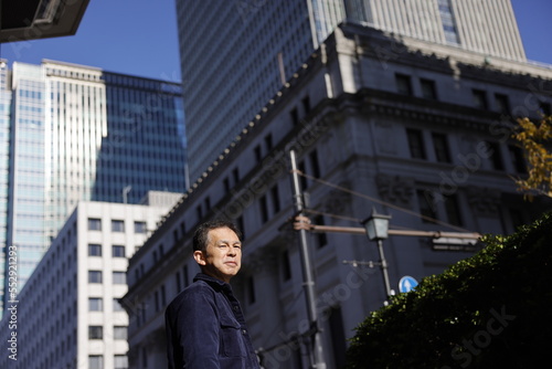 Wallpaper Mural Middle-aged Asian man looking up at blue morning sky with high-rise business building in background. Torontodigital.ca