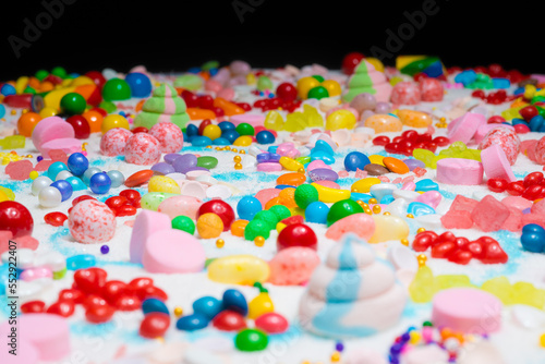Multi-colored candy balls on icing sugar table. Candy sweets background made of assorted chocolate coated and jelly beans. Various shaped delicious sugary treats. Holiday festive background.