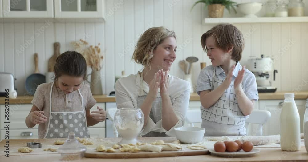 Loving cheerful mother and little children having fun while cooking pastries in cozy kitchen, clapping their hands sprinkling white flour, laughing feel happy, enjoy cookery together. Culinary, hobby Loving cheerful mother and little children having fun while cooking pastries in cozy kitchen, clapping their hands sprinkling white flour, laughing feel happy, enjoy cookery together. Culinary, hobby