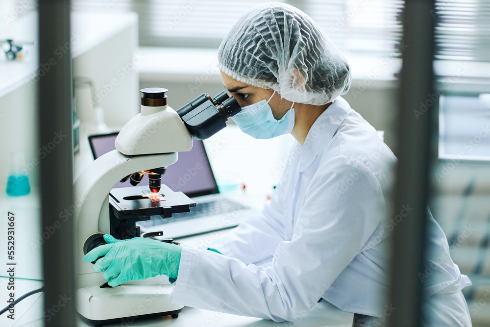 Naklejka premium Side view portrait of young female technician looking in microscope while working in medical lab
