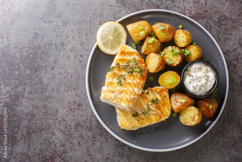 Photography Grilled fish cod fillet with thyme served with baked potatoes, cream sauce and lemon on the table