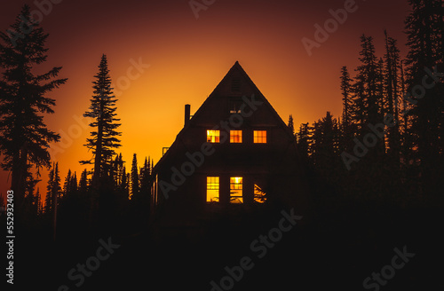 View of cabin in the woods with lit windows at sunset