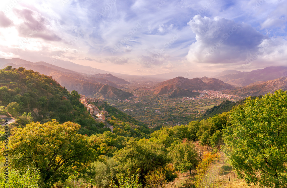 Obraz premium beautiful landscape with amazing view from highland with green slopes and bushes to a valley with town, road and nice mountains and scenic cloudy sunset on background