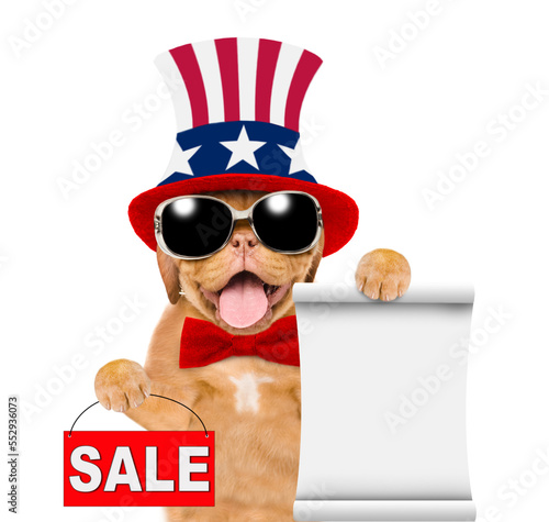 Happy Mastiff puppy wearing like Uncle Sam shows empty list and  signboard with labeled "sale". isolated on white background © Ermolaev Alexandr