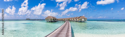 Amazing Maldives, travel panorama. Luxury resort villas seascape with sunny blue sky, tranquil ocean lagoon. Wooden walkway. Tropical paradise inspiration. Wallpaper banner exotic vacation destination © icemanphotos