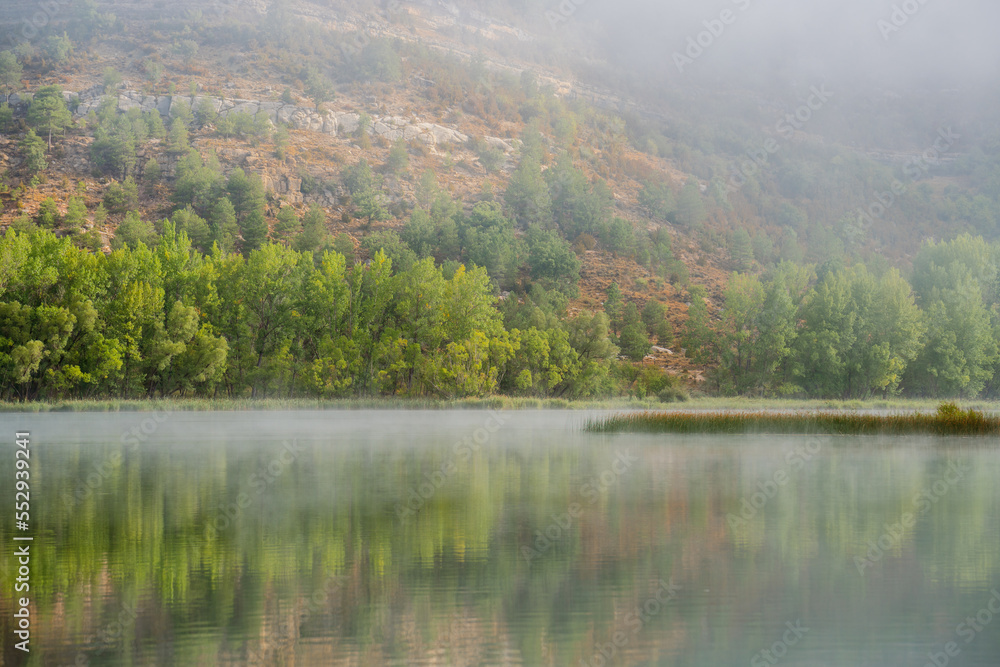 Idyllic landscape about a lake with some fog and surrounded by green trees Idyllic landscape about a lake with some fog and surrounded by green trees