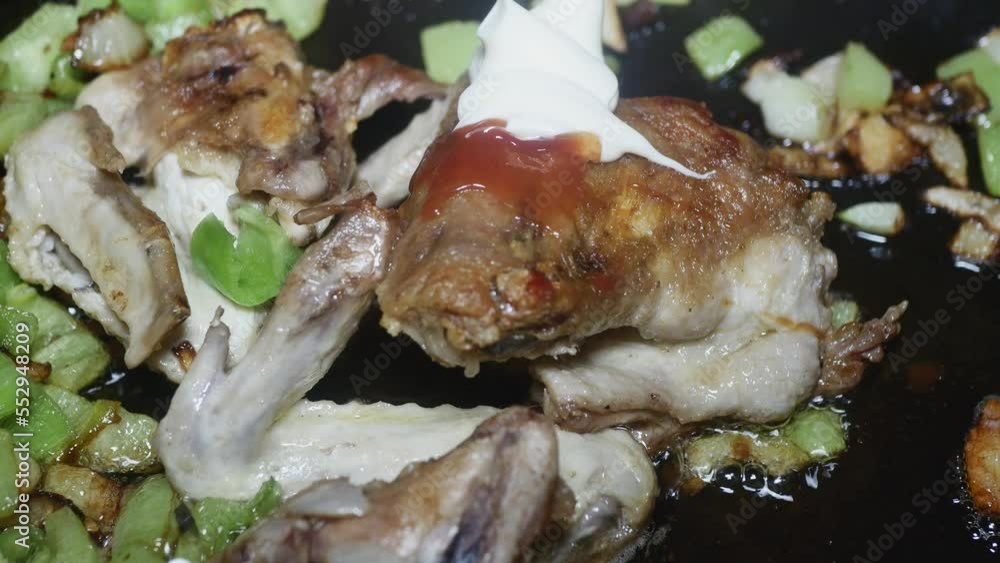adding ketchup to fried wings in a pan with vegetables adding ketchup to fried wings in a pan with vegetables