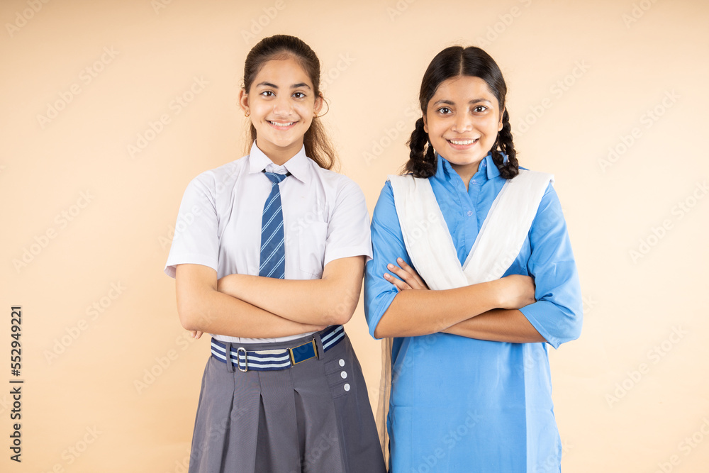 Happy Rural and Modern Indian student schoolgirls wearing school uniform standing together cross arms isolated over beige background, Closeup, Studio shot, Education concept. Happy Rural and Modern Indian student schoolgirls wearing school uniform standing together cross arms isolated over beige background, Closeup, Studio shot, Education concept.