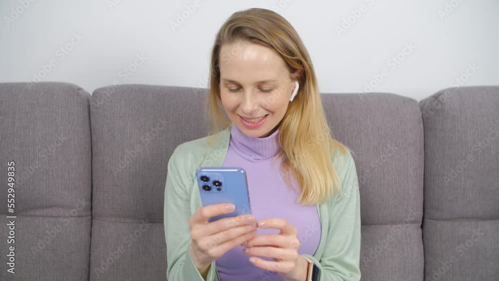 Happy white woman typing a message on a smartphone while listening to music in wireless headphones Happy white woman typing a message on a smartphone while listening to music in wireless headphones