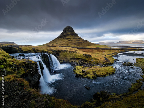 Waterfall with cloudy sky and green grass in Iceland. Kirkjufell.