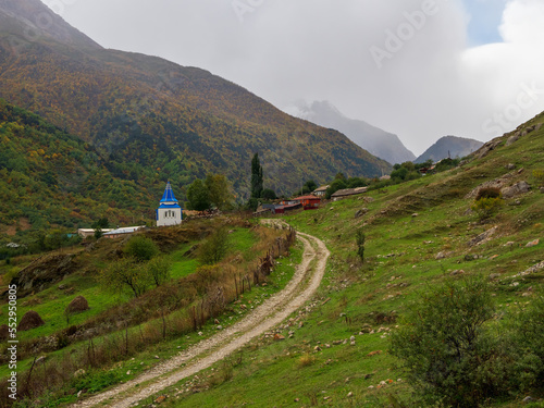 Dirt road to beautiful rainy mountains. Chapel in honor of the dead. In honor of the Icon of the Mother of God, the Recovery of the Dead chapel. Irafsky district, Stur-Digora village. Russia. photo