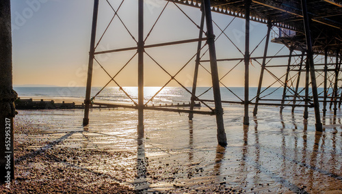 Sunrise viewed from under a pier with reflections on the beach.