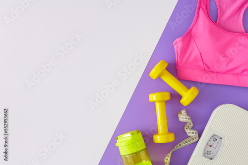 Slimming concept. Top view photo of scales dumbbells bottle of water tape measure pink sports top on white and violet background with copy space. Minimal fitness idea.