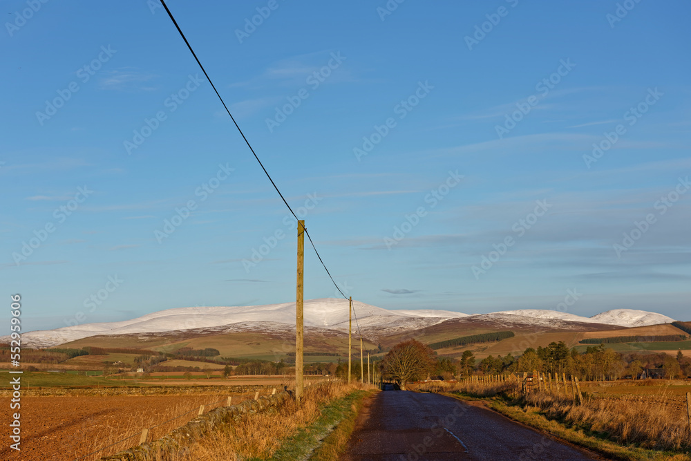 The small minor Scottish Road to the Angus Glens just outside Brechin, running between Farmers Fields and Farm Buildings in the lowlands.