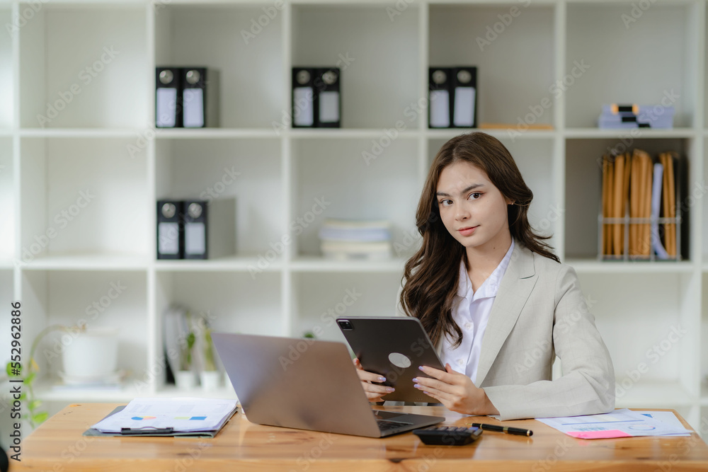 Female accountant working in financial accounting analyzing charts using laptop calculator with documents and holding pen with coffee cup in real estate office Female accountant working in financial accounting analyzing charts using laptop calculator with documents and holding pen with coffee cup in real estate office