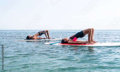 Woman man sup yoga. Happy young sporty couple practising yoga pilates on paddle sup surfboard. Female stretching doing workout on sea water. Modern family outdoor summer sport activity. © panophotograph