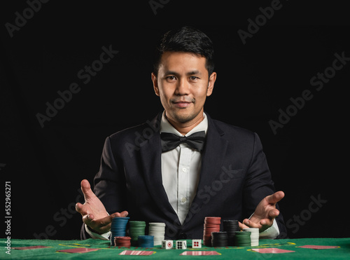 Asian man dealer or croupier shuffles poker cards betting in casino on black background of green table, Dealer man invitation bet playing cards. Casino, poker, poker game concept.
