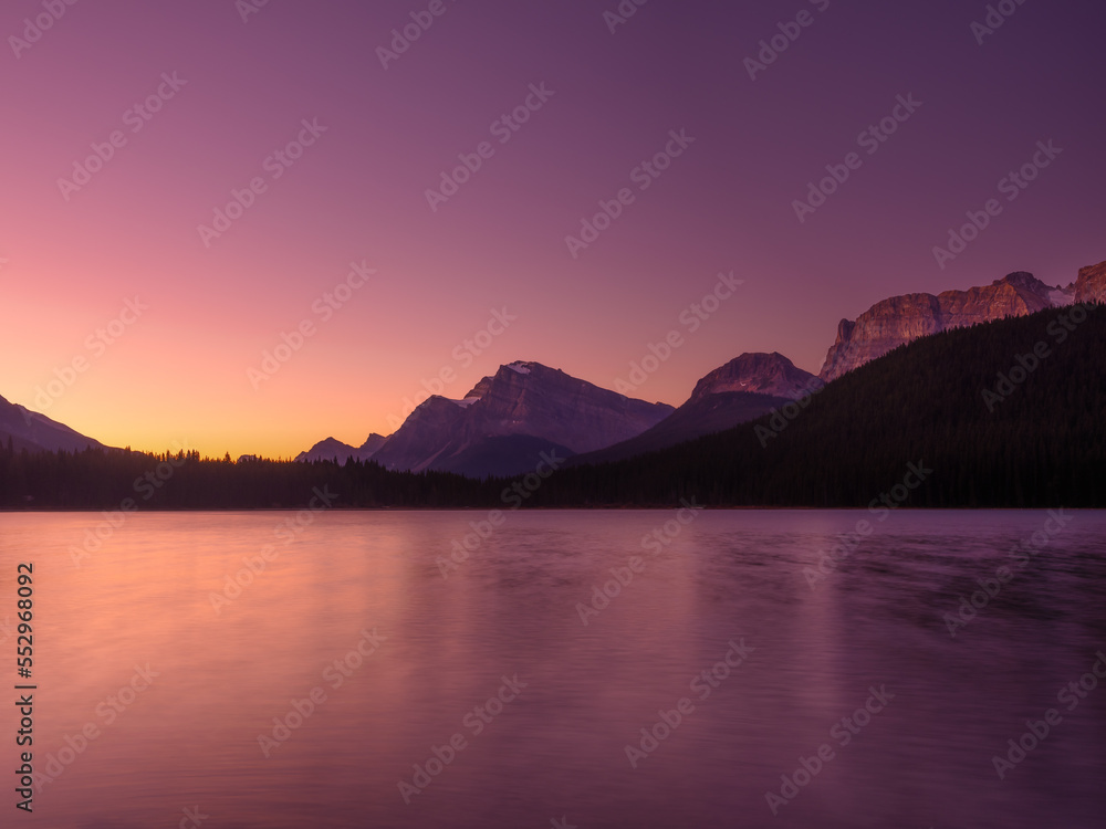 Mountain landscape at dawn. Sunbeams in a valley. Lake and forest in a mountain valley at dawn. Natural landscape with bright sunshine. High rocky mountains. Banff National Park, Alberta, Canada. Mountain landscape at dawn. Sunbeams in a valley. Lake and forest in a mountain valley at dawn. Natural landscape with bright sunshine. High rocky mountains. Banff National Park, Alberta, Canada.