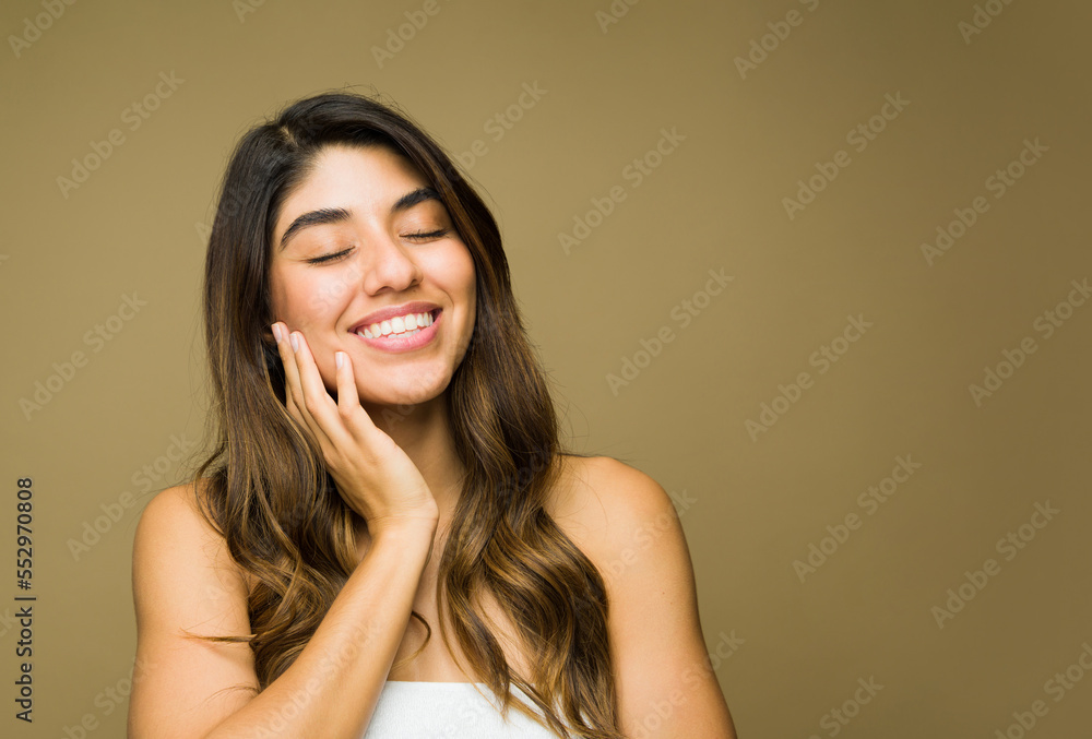 Happy young woman feeling her face after doing a skin care routine Happy young woman feeling her face after doing a skin care routine