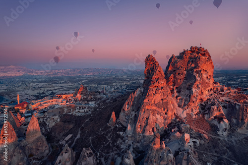 Ancient town of Uchisar castle with hot air balloons at sunset Goreme national park, Cappadocia Turkey, aerial top view