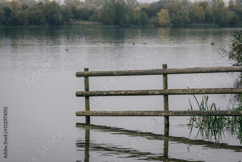 Then end of a line of fencing trails off into a lake. A few ducks swimming in the background