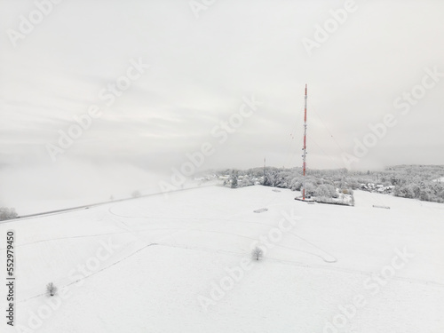 Aerial photo of radio and TV mast in front of wall of fog in snow on hillside