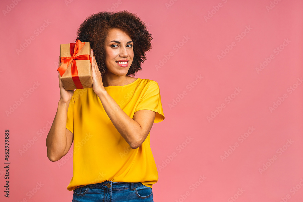 Happy young beautiful african american lady in casual laughing while holding present isolated over pink background. Happy young beautiful african american lady in casual laughing while holding present isolated over pink background.