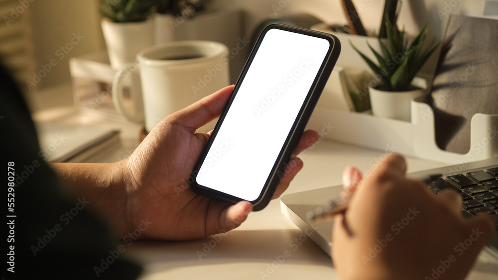 Close up view of woman hands holding smart phone over working desk. Blank screen for your advertise design..