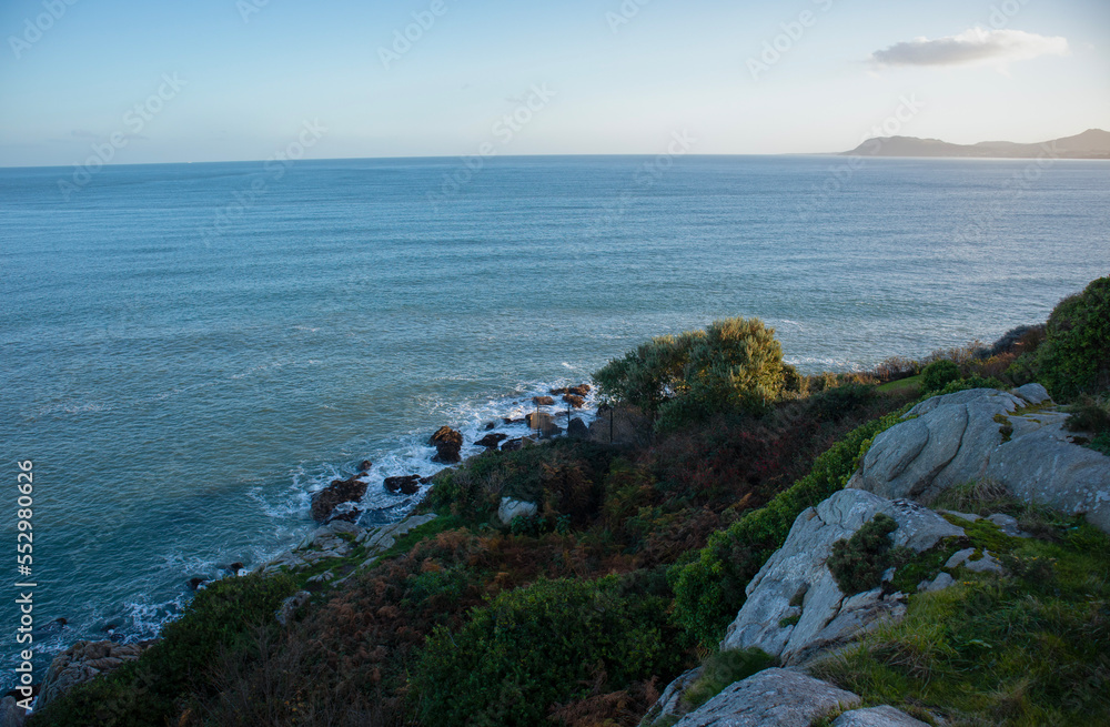 View of Irish coastline in Dalkey near Dublin bay during sunset with boulders and mountains on the background