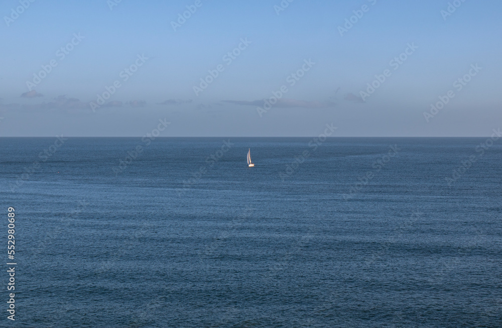 Secluded, single white yacht sailing in the middle of of a vast dark blue ocean, some clouds and blue sky on the horizon