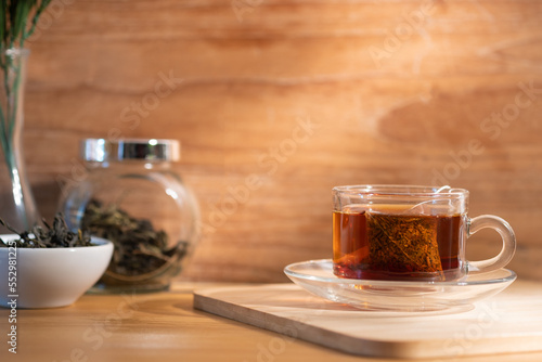 A glass cup of healthy herbal tea on wooden board with soft sunlight shining into a warm atmosphere.