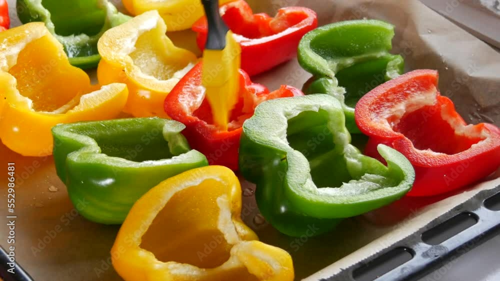 Paprika halves of yellow, red, green color with spices, a female hand smears sunflower oil with a special silicone kitchen brush, lie on a baking sheet parchment Paprika halves of yellow, red, green color with spices, a female hand smears sunflower oil with a special silicone kitchen brush, lie on a baking sheet parchment