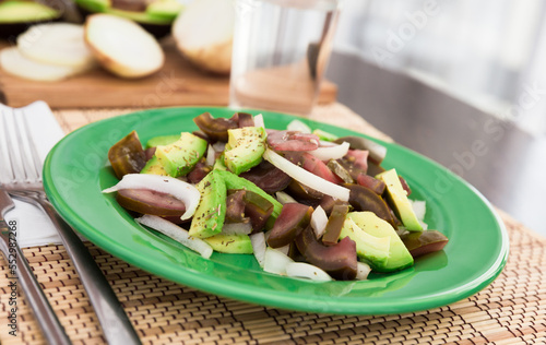 salad of black tomatoes, avocado and onions on green plate