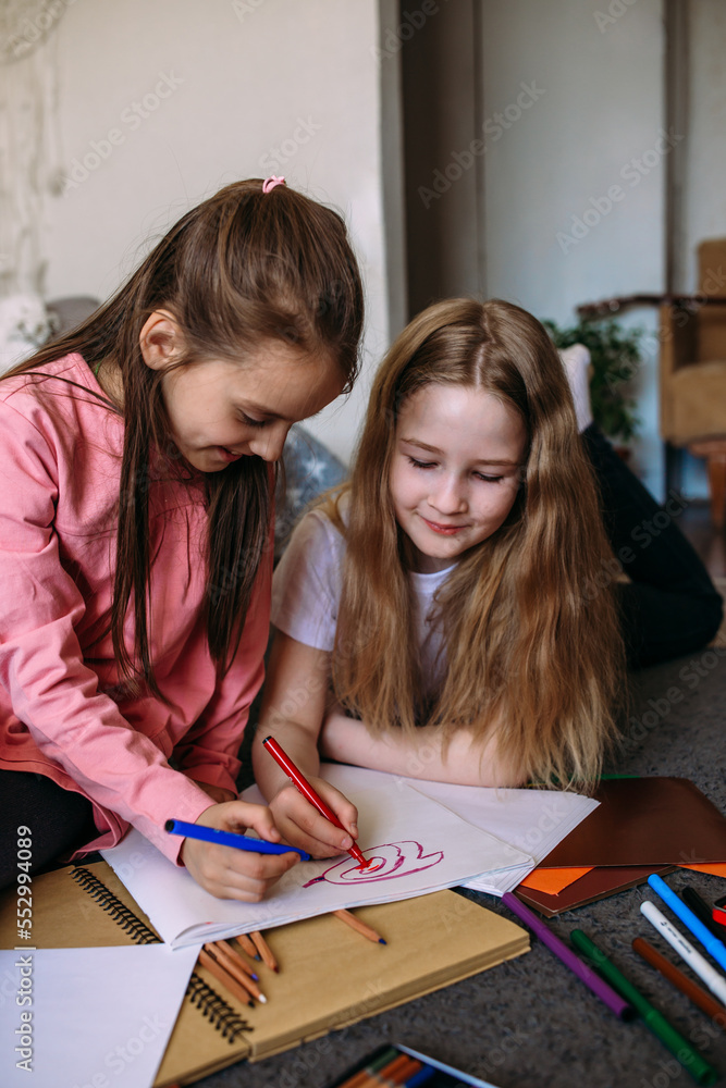 Two girls friends play at home, draw with pencils and felt-tip pens and have fun Two girls friends play at home, draw with pencils and felt-tip pens and have fun