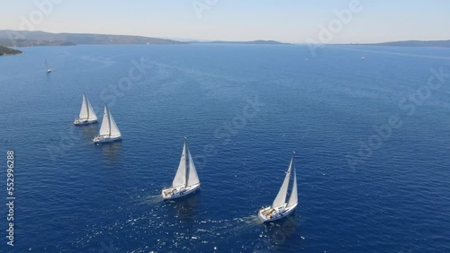 Aerial view flying over yachts competing with each other from the mediterranean sea in croatia on a bright sunny day against the backdrop of a picturesque green island. white yachts sail beautifully a photo