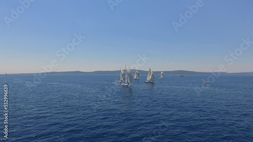 Aerial view flying over yachts competing with each other from the mediterranean sea in croatia on a bright sunny day against the backdrop of a picturesque green island photo