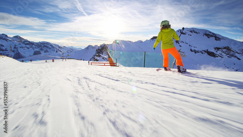 Girl snowboarding on slopes in the Swiss alps. Sun rays and flare visible.