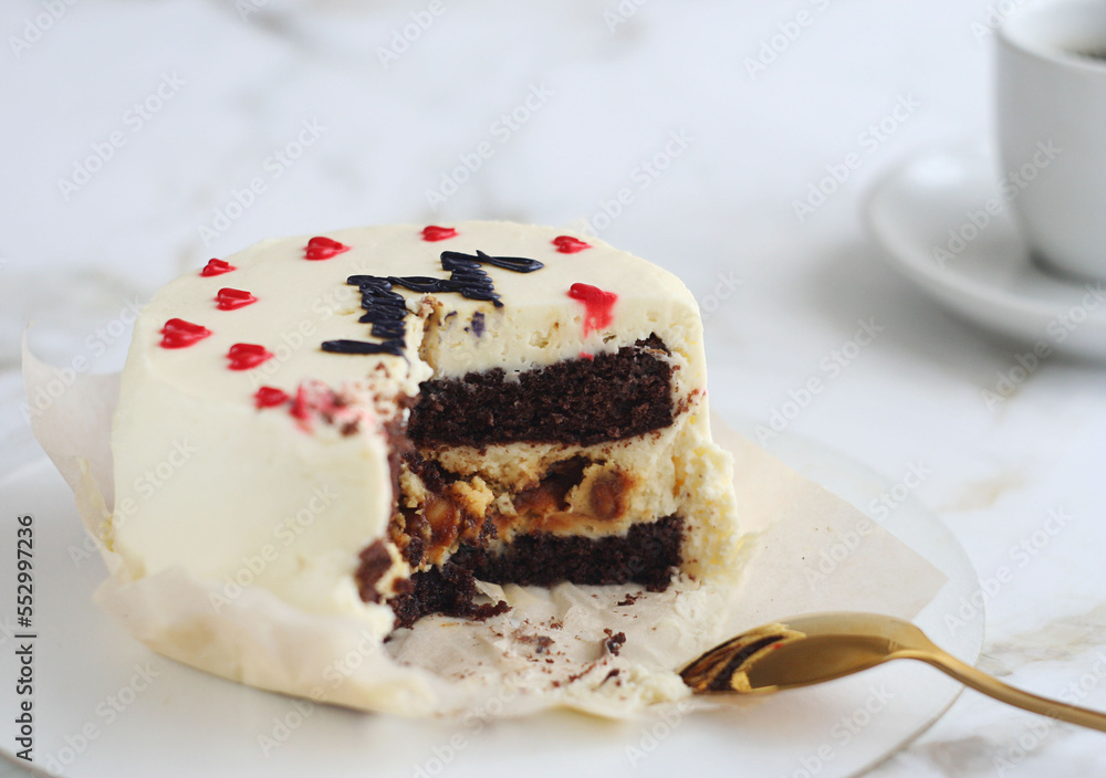 A cake with chocolate stands on a light marble table. Behind is a cup of coffee. A cake with chocolate stands on a light marble table. Behind is a cup of coffee.
