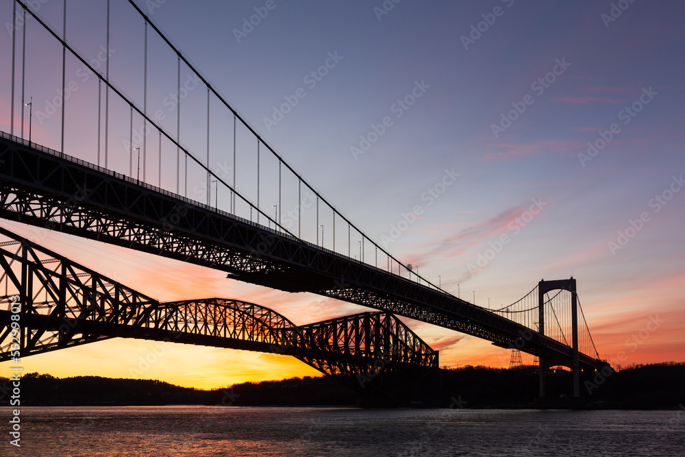 Fototapeta premium Low angle view of the 1970 suspension Pierre-Laporte Bridge and 1919 steel truss Quebec Bridge over the St. Lawrence River seen during sunrise, Quebec City, Quebec, Canada