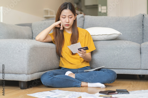 Financial people, owe asian woman, girl sitting on floor at home, hand holding credit card and bills, stressed  by calculate expense, no money to pay, mortgage or loan. Debt, bankruptcy or bankrupt.