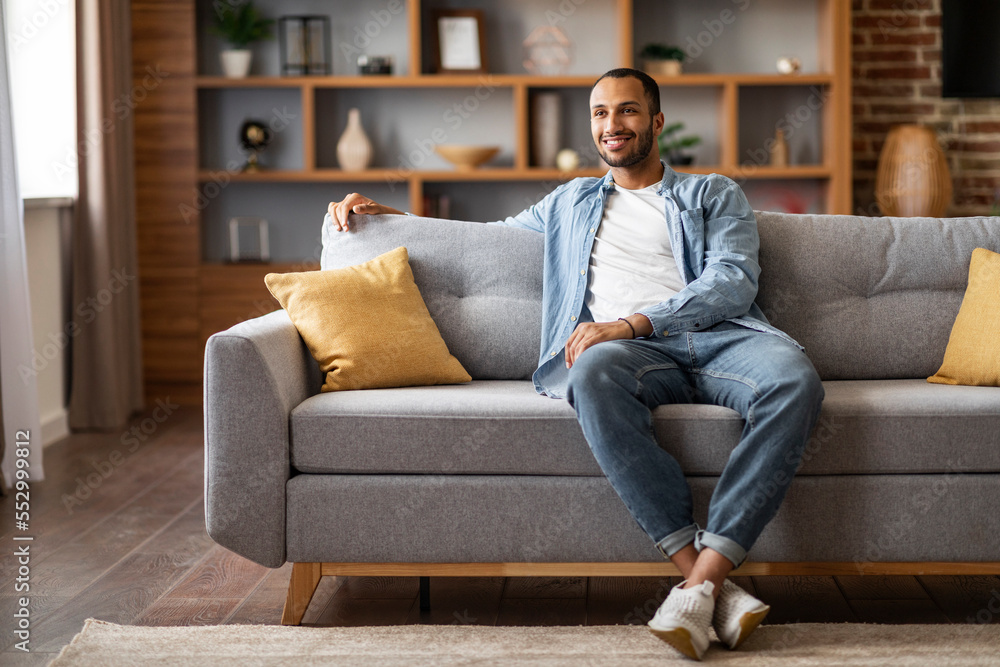 Domestic Comfort. Smiling Young Black Man Resting On Sofa In Living Room Domestic Comfort. Smiling Young Black Man Resting On Sofa In Living Room