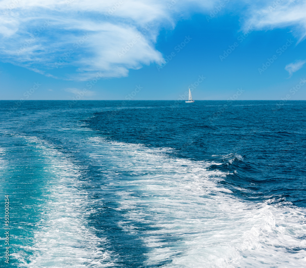 Trace tail of speed boat or ferry on water surface in the sea and white sailing vessel in far. Natural and vacation background.