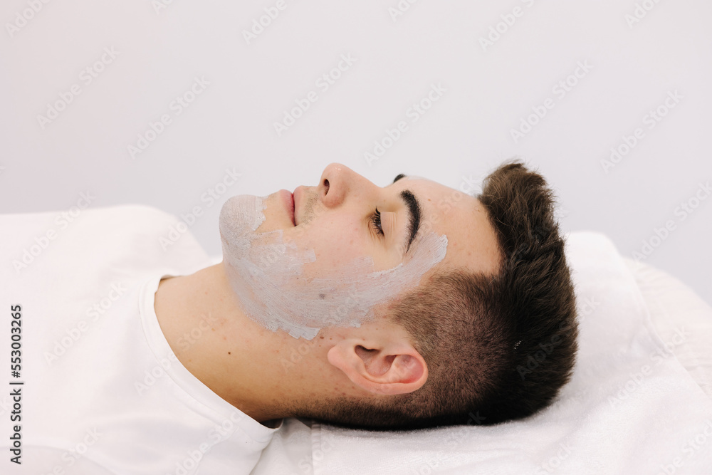 Cosmetologist applying clay mask on man's face in spa salon. Side view of male face during procedure. Cosmetologist applying clay mask on man's face in spa salon. Side view of male face during procedure.
