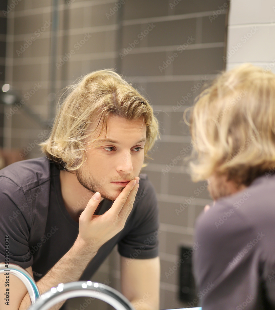 young man looking in the mirror,combing his hair,looking at problems on face. young man looking in the mirror,combing his hair,looking at problems on face.