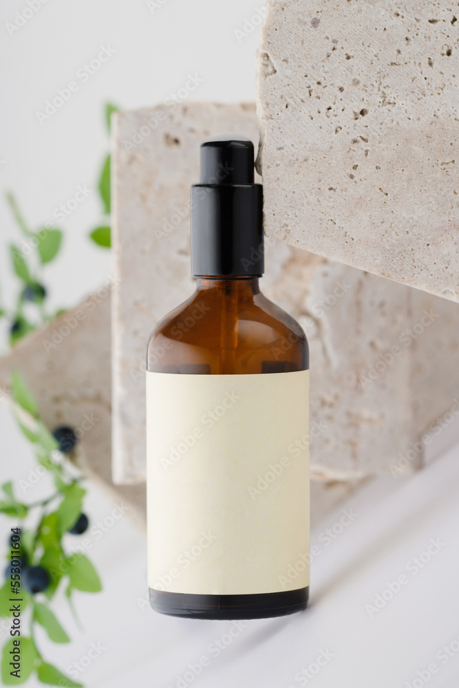 Brown glass bottle with a pump for cosmetics. Beige empty label. Against the background of travertine stones.