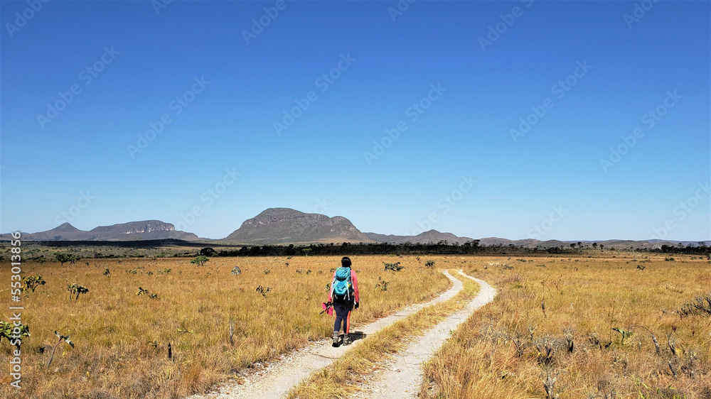 woman walking on a trail in the savannah with mountains in the background and blue sky