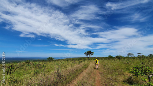 man walking on a trail through the fields under the blue sky with beautiful clouds