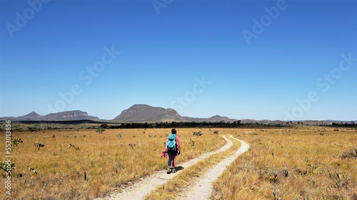 woman walking on a trail in the savannah with mountains in the background and blue sky