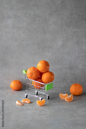 Whole tangerines in a shopping cart on a gray background.