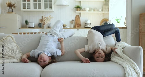 Cute little girl and boy having fun together, fooling around lying upside down on cozy sofa in living room looking carefree and happy enjoy playtime indoor. Playful children spend lazy leisure at home